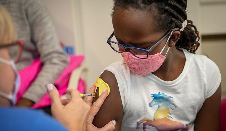 Young girls looks at arm while a nurse is giving her a vaccine and using a ShotBlocker.