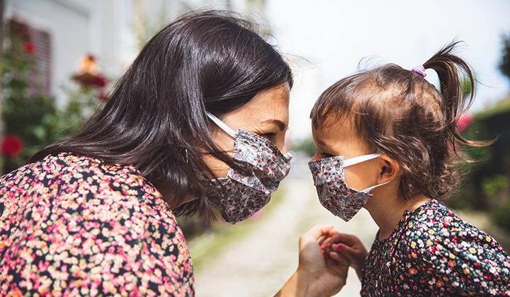 Mom wears a face mask and leans in close to child wearing a face mask.