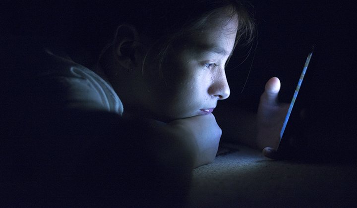 Teen girl with mobile phone screen glowing while sitting in the dark.