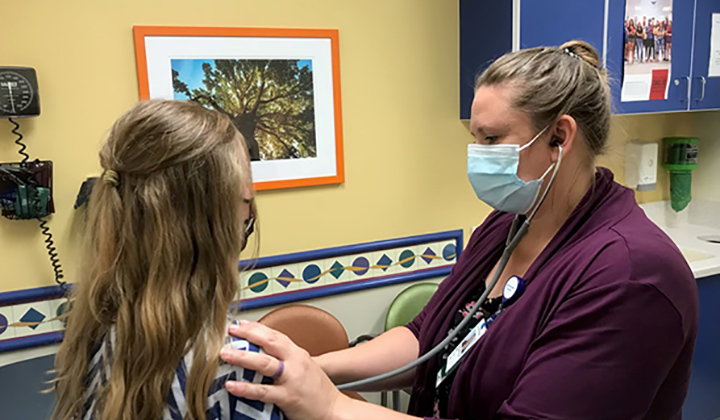 Young patient with back to camera gets hear heart listened to by a doctor in a clinic room.