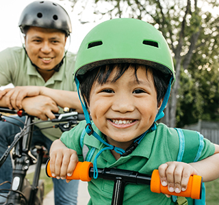Child on bike smiling with Dad following behind