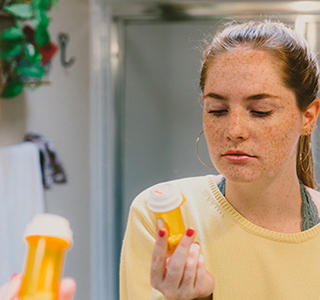 Young teen looks at a pill bottle while in front of a mirror.