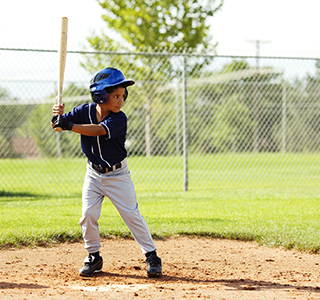 Young boy wears blue baseball uniform and holds bat over the plate while looking at the mound.