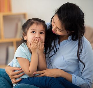 Child covering her mouth while mom looks at her - Parent-ish parenting blog