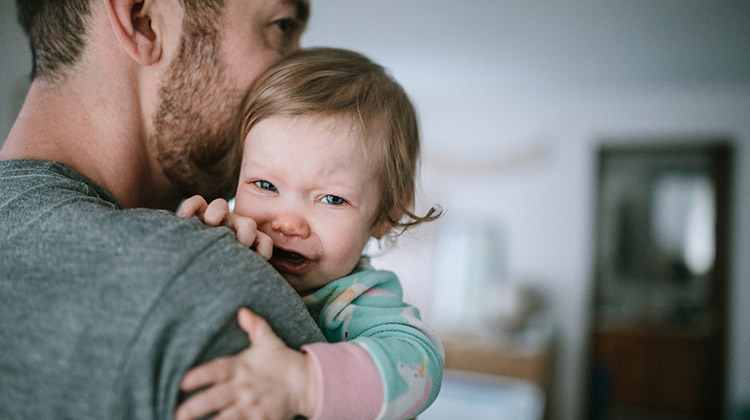 A dad holds his baby girl, trying to comfort her in the midst of her sickness.