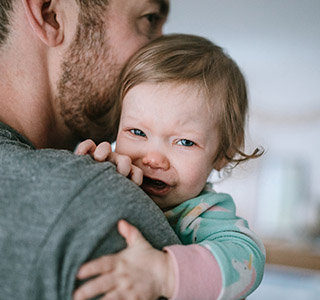 A dad holds his baby girl, trying to comfort her in the midst of her sickness.