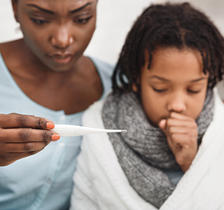 Mom looks worried as she reads a thermometer next to her coughing child.