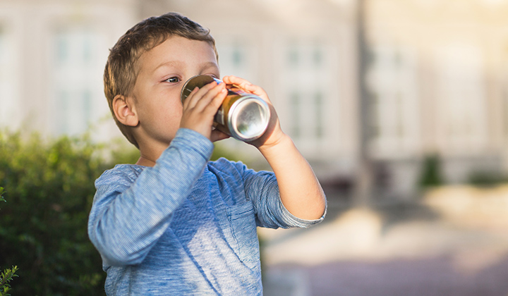 Young boy drink a soda can using both hands.