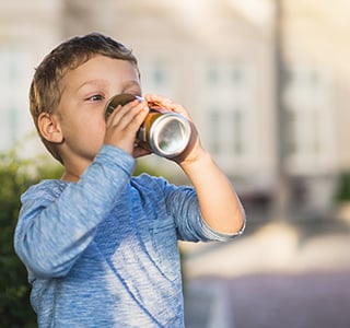 Young boy drink a soda can using both hands.