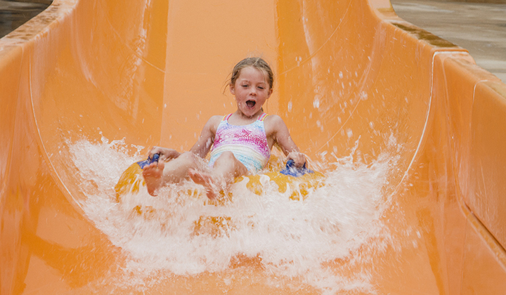 Young girl rides an inflatable tube down a waterpark slide.