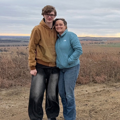 Tall male teen standing outside with Mother in blue sweater.