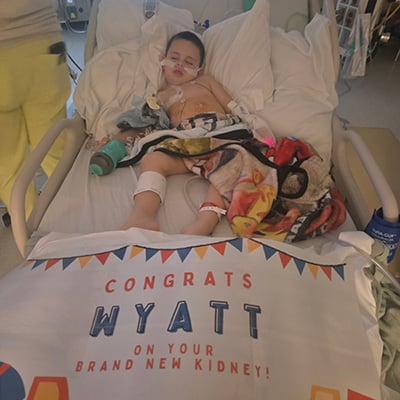 Child resting in a hospital bed with a banner reading “Congrats Wyatt on your brand new kidney”