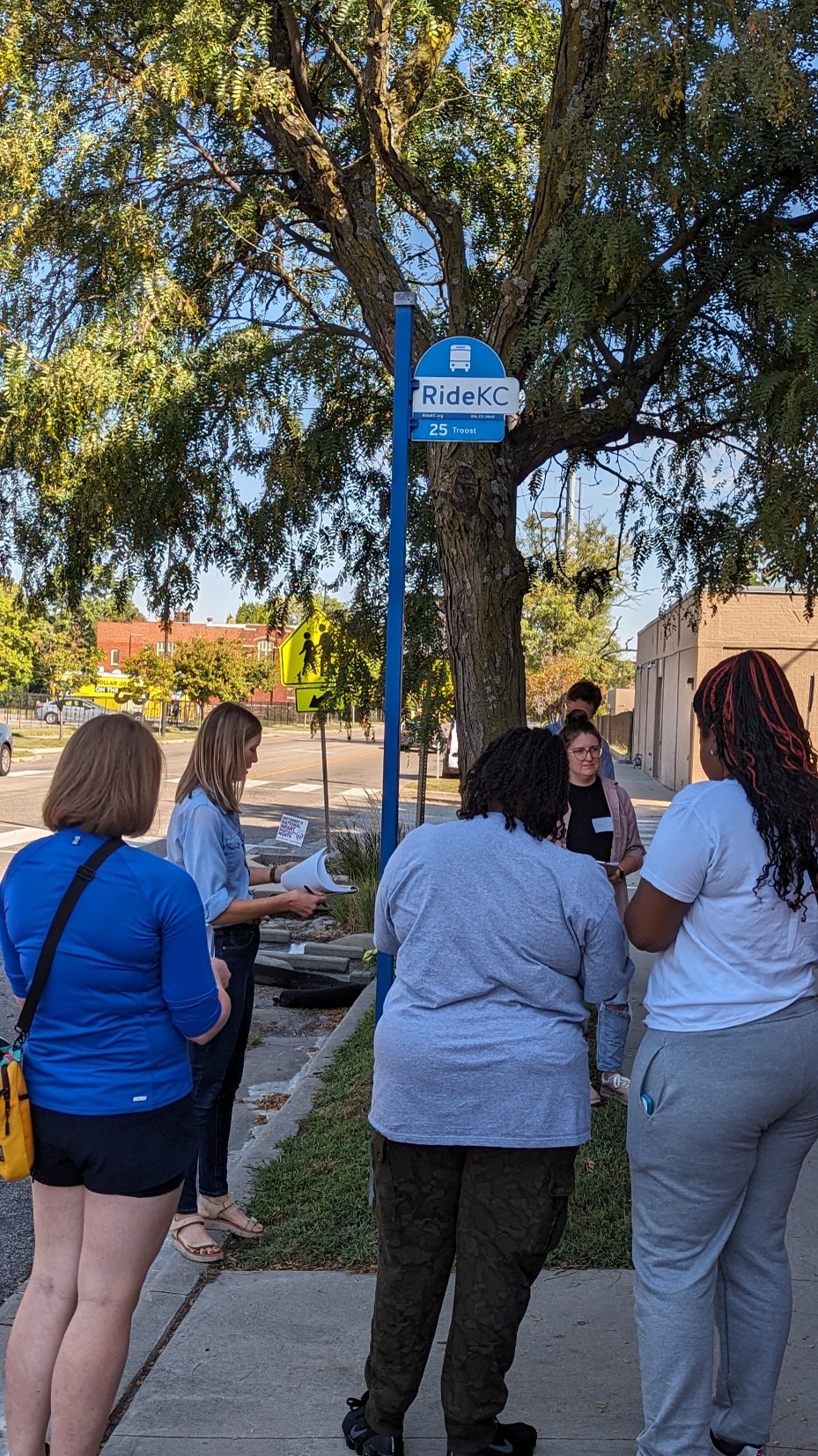 Community members receiving training from Drs. Carlson and Grimes for conducting the assessments around bus stops. They stand outside by a bus stop.