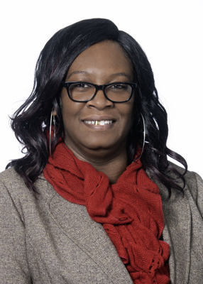 RJ Brooks. She has dark colored hair and is wearing glasses. She is wearing red scarf and a light brown jacket. 