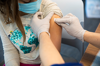 Two gloved hands rubbing a child's arm with an alcohol pad at Children's Mercy.